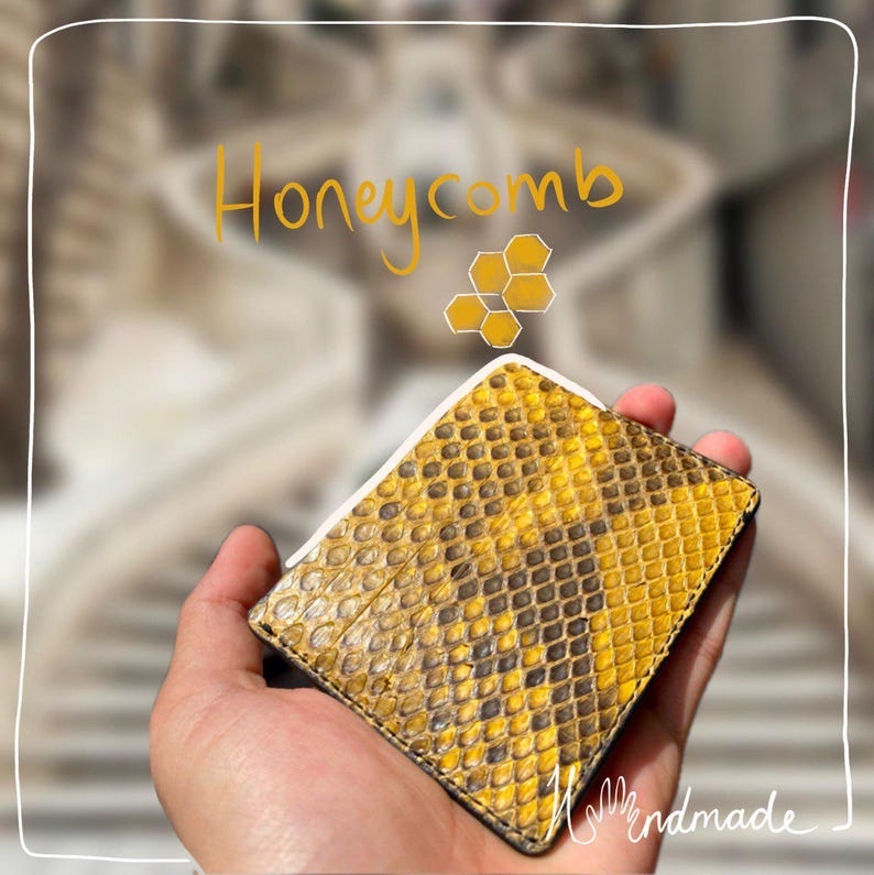 May include: A yellow and brown honeycomb-patterned wallet with a white border. The wallet is held in a hand. The word "Honeycomb" is written in yellow cursive above the wallet. The word "handmade" is written in white cursive at the bottom.