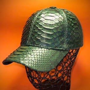 Può includere: Un cappello da baseball verde in pelle di serpente con visiera curva. Il cappello è realizzato in vera pelle e presenta un motivo unico e testurizzato.