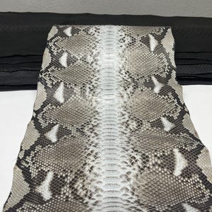 以下が含まれることがあります： グレー、白、茶色の自然な模様のヘビ革。 ヘビ革は折りたたまれ、質感のある鱗と独特の模様が明らかになっています。 背景には黒い革の山があります。