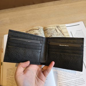 Puede incluir: Cartera de cuero negro abierta con m&uacute;ltiples ranuras para tarjetas y una superficie texturizada. La cartera se sostiene abierta, revelando los compartimentos interiores. Las palabras "Special Wallet" son visibles en una tarjeta dentro.
