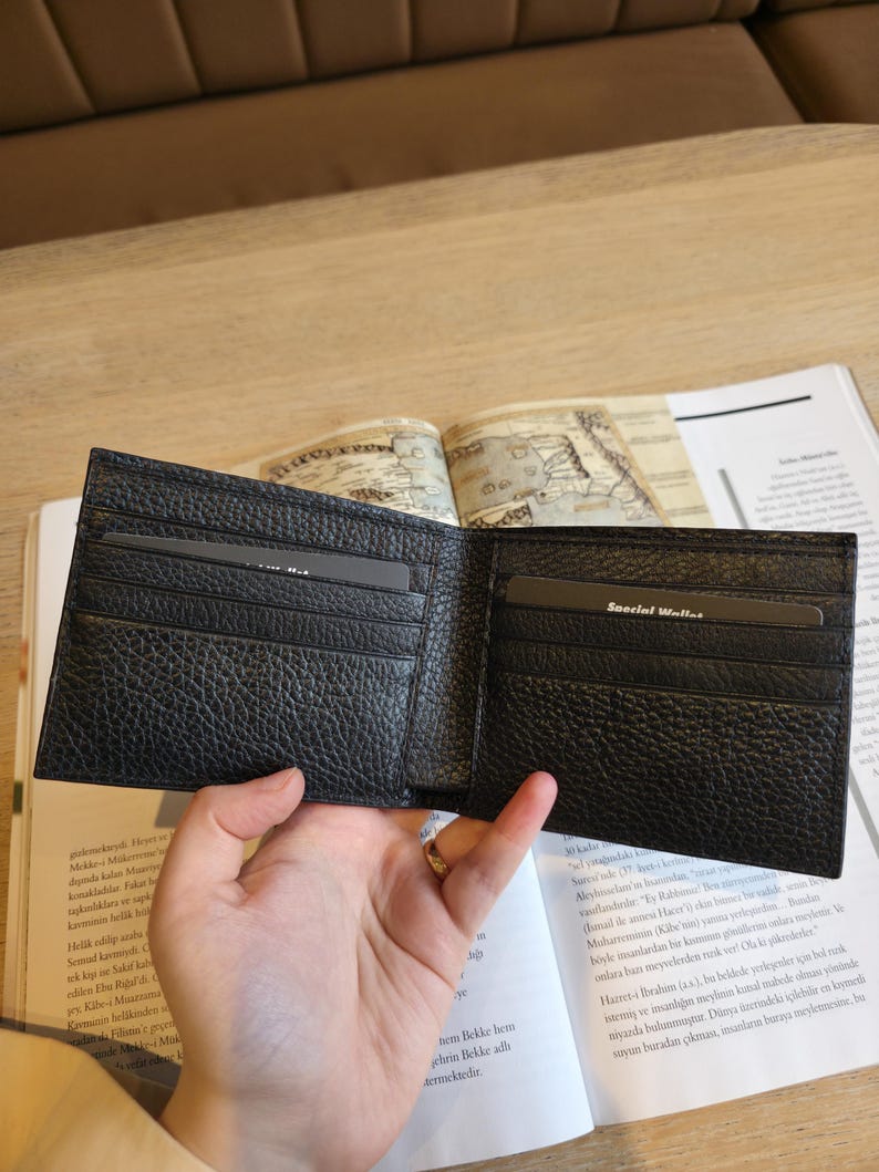 Puede incluir: Cartera de cuero negro abierta con m&uacute;ltiples ranuras para tarjetas y una superficie texturizada. La cartera se sostiene abierta, revelando los compartimentos interiores. Las palabras "Special Wallet" son visibles en una tarjeta dentro.