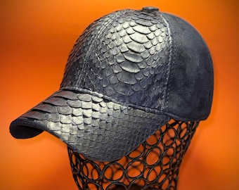 May include: A dark blue baseball cap with a textured, scaly pattern on the front panels and bill. The back of the cap is a smooth, dark blue suede material. The cap is displayed on a black wire form against an orange background.
