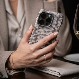 Könnte beinhalten: Eine Smartphone-Hülle mit einer strukturierten, grau-weißen Schlangenhaut-Optik. Die Hülle bedeckt die Rückseite und die Seiten des Geräts und verfügt über einen präzisen Ausschnitt für das Dreifach-Kamerasystem und den Blitz.
