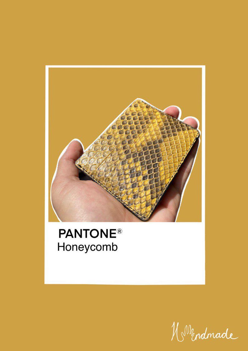 May include: A rectangular wallet with a yellow and brown snakeskin pattern. The image is set against a mustard-yellow background with the text "PANTONE&reg; Honeycomb". The wallet appears to be made of leather. The background is a shade of yellow.