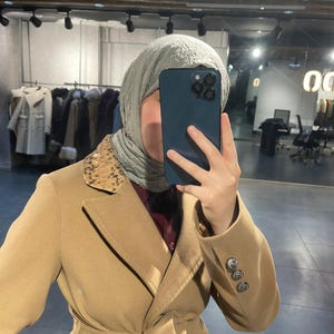 Op de afbeelding: Een bruin jas met een dubbel borstontwerp en een riem. De jas heeft decoratieve knopen op de mouwen en een patroonkraag. De jas wordt gedragen over een bordeauxrood overhemd.