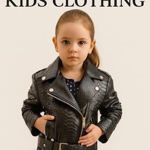 Może przedstawiać: Młoda dziewczyna w czarnej kurtce ze sztucznej skóry o fakturze skóry węża, ze złotym zamkiem błyskawicznym i paskiem. Kurtka jest połączona z niebieską sukienką w kropki. U góry znajduje się napis "Stylish KIDS CLOTHING".