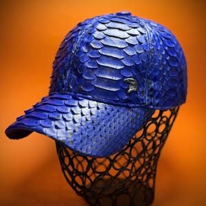 May include: A blue baseball cap made of snakeskin. The cap has a curved brim and a structured crown.