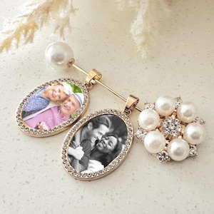 May include: A gold-toned brooch featuring two oval photo charms framed with clear crystals, one displaying a colour photograph of a couple and the other a black and white photograph of a couple, accented by a large pearl and a floral pearl cluster.