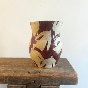 Può includere: Un vaso in ceramica con una smaltatura lucida color marrone rossastro scuro, caratterizzato da un motivo ripetitivo di forme astratte color bianco sporco che ricordano degli uccelli. Il vaso presenta un bordo ampio e leggermente svasato.