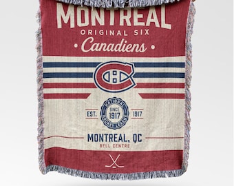 Puede incluir: Una manta tejida roja, blanca y azul con el texto "MONTREAL ORIGINAL SIX Canadiens" y un logotipo. La manta también incluye el texto "NATIONAL HOCKEY LEAGUE" y "MONTREAL, QC BELL CENTRE". Tiene un borde con flecos.