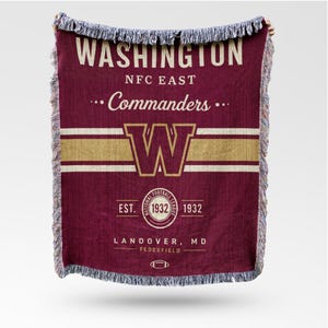 May include: Maroon and gold woven throw blanket with the text "WASHINGTON NFC EAST Commanders" and a large "W" logo. The blanket also includes "EST. 1932" and "LANDOVER, MD FEDEXFIELD". The edges have a fringed trim.