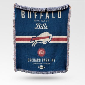 May include: A blue woven throw blanket featuring the text "BUFFALO AFC EAST Bills" in white. The blanket has a red and white stripe, a buffalo logo, and the text "EST. 1960". The bottom of the blanket reads "ORCHARD PARK, NY HIGHMARK STADIUM".