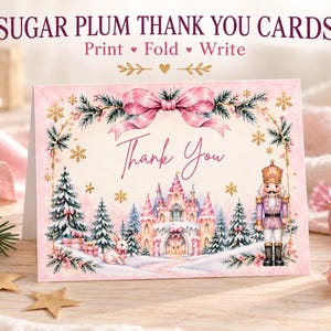 Op de afbeelding: Een gevouwen bedankkaart met een roze en witte winterscène met een kasteel, een notenkraker, een konijn en dennenbomen. De tekst luidt SUGAR PLUM THANK YOU CARDS, Print • Fold • Write, en Thank You in een sierlijk lettertype.