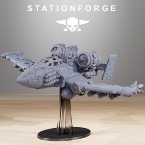 May include: A gray model airplane with intricate details, including multiple engines and wing-mounted weaponry. The model is mounted on a clear stand with a black base. The text "STATIONFORGE" is displayed above the plane.