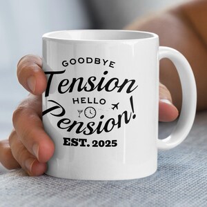 Puede incluir: Taza de cerámica blanca con el texto "Goodbye Tension Hello Pension! EST. 2025" en escritura negra. La taza tiene un asa y la sostiene una persona. El diseño incluye una copa de cóctel, un reloj y un avión.