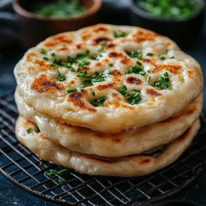 Peut inclure: Une pile de quatre pains plats garnis de ciboulette hachée. Les pains plats sont dorés et légèrement croustillants. La ciboulette est verte et ajoute une touche de couleur au plat.