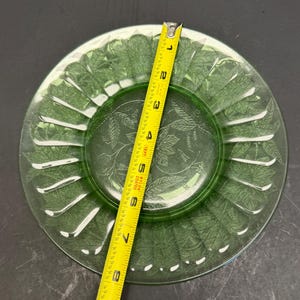 Puede incluir: Un plato redondo de vidrio verde transl&uacute;cido con un patr&oacute;n de hojas en relieve en toda su superficie. Una cinta m&eacute;trica amarilla est&aacute; colocada en el centro, indicando un di&aacute;metro de aproximadamente 21,6 cent&iacute;metros para el plato circular.