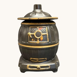 Puede incluir: Un recipiente vintage en forma de estufa de hierro fundido negro con tapa. El recipiente tiene forma de barril con detalles dorados alrededor de la ventana y la base. La ventana tiene un marco dorado y un interior rojo y naranja.