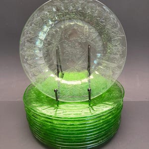 Puede incluir: Una pila de platos redondos de vidrio verde transl&uacute;cido con un patr&oacute;n floral de flor de pascua en relieve en la superficie. Los platos tienen un borde circular liso y un tono verde vibrante y consistente en todo el material.
