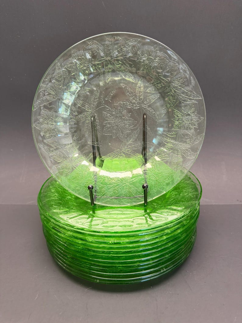 Puede incluir: Una pila de platos redondos de vidrio verde transl&uacute;cido con un patr&oacute;n floral de flor de pascua en relieve en la superficie. Los platos tienen un borde circular liso y un tono verde vibrante y consistente en todo el material.