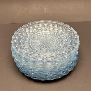 Könnte beinhalten: Ein Stapel von sechs hellblauen Glasplatten. Jede Platte hat ein strukturiertes, blasenartiges Muster am Rand und ein geprägtes Mitteldesign. Die Platten sind übereinander gestapelt und zeigen ihre komplizierten Details.