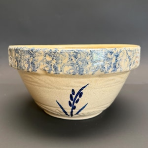 Puede incluir: Un cuenco de gres color crema con un borde moteado azul y un diseño de espiga de trigo azul. El cuenco tiene una forma ancha, ligeramente acampanada y es probablemente vintage o antiguo.