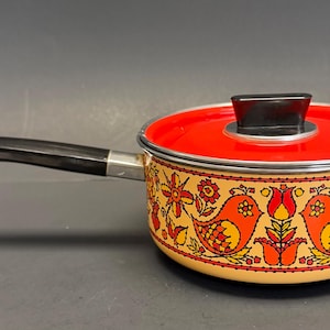 May include: A vintage saucepan with a red lid and a black handle. The pot features a decorative band with orange birds and floral patterns. The handle is black, and the lid has a black knob.