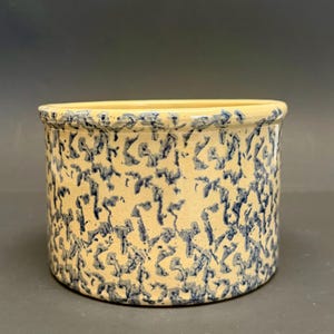 Könnte beinhalten: Ein zylindrischer Steinguttopf mit hellbeigem Grund und einem Muster aus dunkelblauen, abstrakten Formen. Der Rand ist hellbeige. Dieser Vintage-Küchenartikel wird wahrscheinlich zur Aufbewahrung von Lebensmitteln verwendet.
