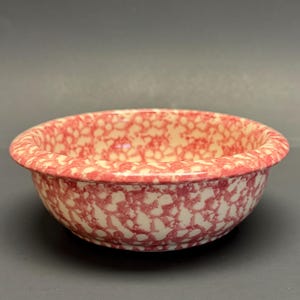 May include: A round, ceramic bowl with a speckled pattern in red and cream. The bowl has a slightly flared rim and a smooth, glossy finish. This vintage-style bowl is suitable for serving or display.