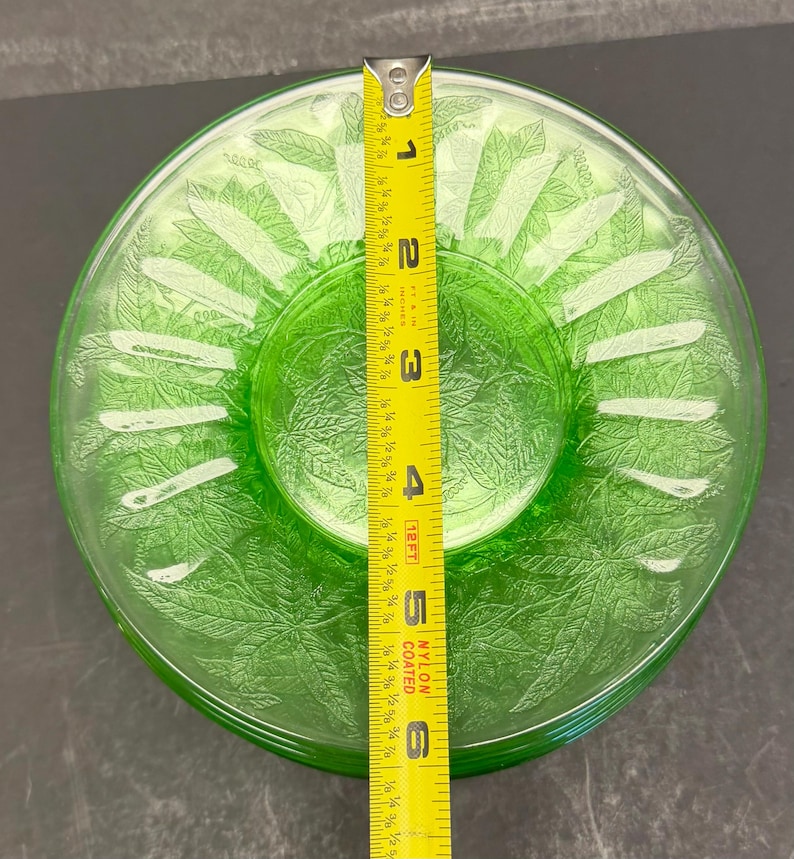 Puede incluir: Un plato redondo de vidrio verde transl&uacute;cido con un patr&oacute;n de hojas en relieve en toda su superficie. Una cinta m&eacute;trica amarilla est&aacute; colocada en el centro, indicando un di&aacute;metro de aproximadamente 15,24 cm para este plato decorativo.