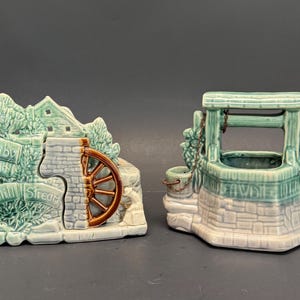 Può includere: Due pezzi decorativi in ceramica con smalto verde chiaro e bianco. Un pezzo raffigura un mulino ad acqua con una ruota marrone e la scritta Down by the Old Mill Stream. Il secondo pezzo è un pozzo dei desideri con un secchiello attaccato da una catena.