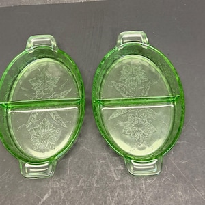 Puede incluir: Dos platos divididos de vidrio verde claro con forma ovalada y asas integradas en cada extremo. La base interior de cada plato muestra un patr&oacute;n floral moldeado con hojas y p&eacute;talos detallados, creando una superficie texturizada en el vidrio.