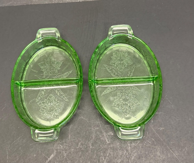 Puede incluir: Dos platos divididos de vidrio verde claro con forma ovalada y asas integradas en cada extremo. La base interior de cada plato muestra un patr&oacute;n floral moldeado con hojas y p&eacute;talos detallados, creando una superficie texturizada en el vidrio.