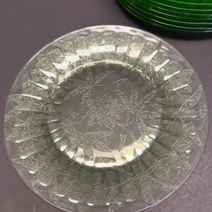 Puede incluir: Un plato de vidrio transparente con un patr&oacute;n floral en relieve de flores y hojas de pascua en toda la superficie. El plato tiene un borde festoneado y un borde ligeramente elevado. Se ve una parte de un objeto de vidrio verde oscuro.