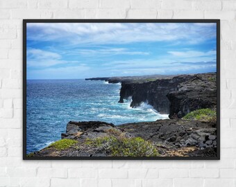 May include: A framed photograph of a coastal landscape. The image shows dark, rocky cliffs meeting the turquoise sea under a blue sky with wispy clouds. Waves crash against the cliffs, creating white foam.