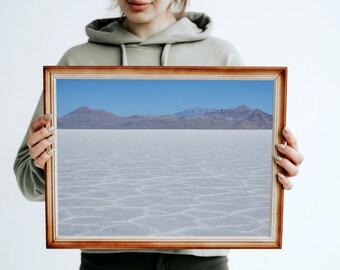 May include: A framed landscape photograph featuring a vast, white salt flat under a clear blue sky. Distant mountains are visible on the horizon. The wooden frame has a warm, reddish-brown tone.