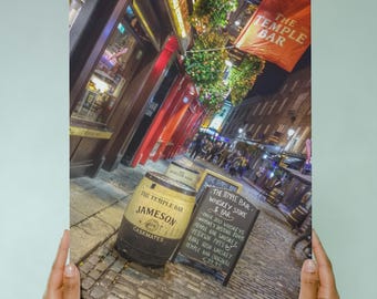 May include: An image of The Temple Bar in Dublin, Ireland, at night. The scene includes a whiskey barrel with "Jameson" branding, a chalkboard menu, and a red flag with "The Temple Bar" text. The cobblestone street is illuminated by streetlights.