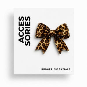 Könnte beinhalten: Eine Schleife mit Leopardenmuster auf weißem Hintergrund. Die Schleife ist braun und schwarz mit einer klassischen Schleifenform. Das Wort "ACCESSORIES" ist vertikal auf der linken Seite aufgedruckt, und "BUDGET ESSENTIALS" ist unten aufgedruckt.