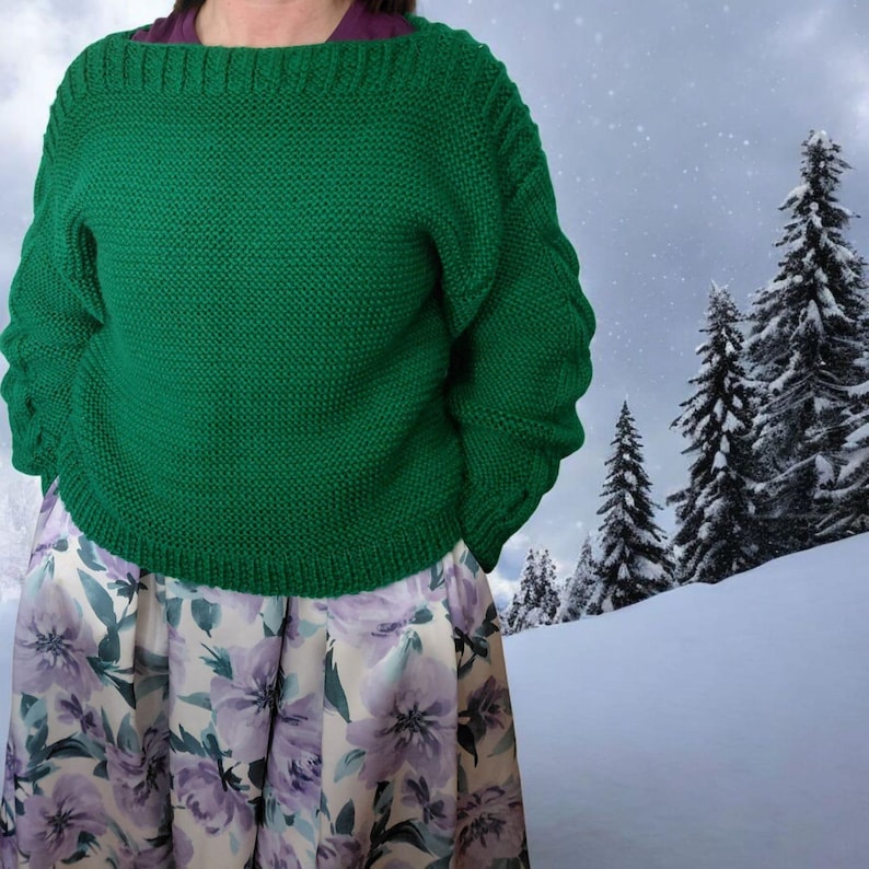 Pode incluir: Um su&eacute;ter verde de malha com decote largo e mangas compridas. O su&eacute;ter &eacute; combinado com uma saia com estampa floral com flores roxas e brancas. O fundo mostra uma paisagem nevada com &aacute;rvores perenes.