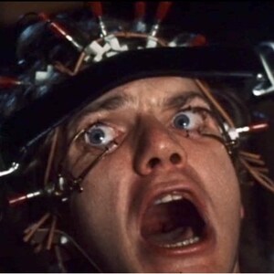 May include: A close-up of a person's face with wires attached to their head and eyes. The person is screaming with their mouth open wide. The wires are connected to a device that is attached to their head.
