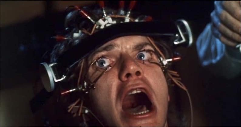 May include: A close-up of a person's face with wires attached to their head and eyes. The person is screaming with their mouth open wide. The wires are connected to a device that is attached to their head.