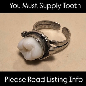 May include: An adjustable silver-toned metal ring featuring a white tooth as the central setting. The text at the top reads You Must Supply Tooth and the text at the bottom reads Please Read Listing Info. The band has a split design.
