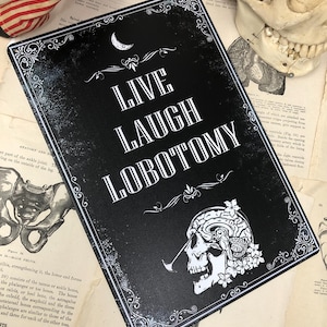 May include: Black and white metal sign with a skull and brain design. The sign reads "Live Laugh Lobotomy" with a crescent moon above the text.