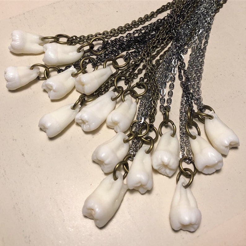 May include: A necklace with multiple charms shaped like teeth, each hanging from a separate chain. The chains are a mix of silver and brass.