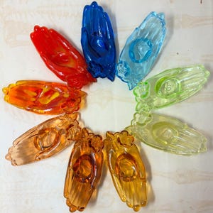 May include: A collection of colorful, hand-shaped glass ornaments in a circular arrangement. The ornaments are in shades of red, orange, yellow, green, blue, and clear. Each ornament has a detailed hand design.