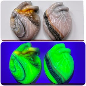 Puede incluir: Dos esculturas en forma de corazón. El par superior presenta una mezcla de colores gris, marrón y blanco. El par inferior brilla en verde brillante bajo luz negra, con patrones arremolinados de amarillo y verde oscuro.