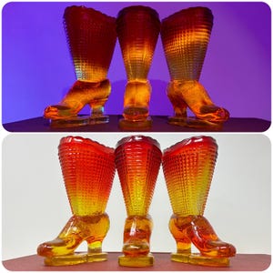 Puede incluir: Tres jarrones de vidrio ámbar con forma de bota. Las botas tienen un patrón texturizado y un degradado de color, que va del rojo en la parte superior al amarillo en la base. Las botas se exhiben sobre una superficie roja con un fondo púrpura.