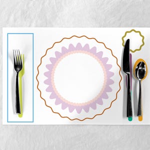 May include: A white placemat with a decorative plate design and a place setting. The place setting includes a black fork and a green fork, a knife, and a spoon. The plate design has a brown scalloped edge and a pink and white center.