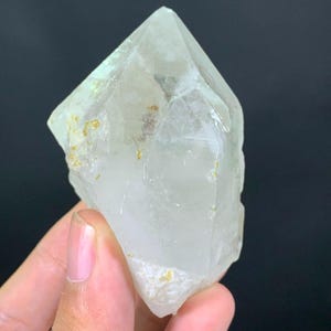 Peut inclure: Un spécimen de cristal de quartz pointu et transparent présentant des fractures internes naturelles et de petites inclusions minérales de couleur dorée. Le cristal a une forme hexagonale avec une pointe terminale nette et définie.