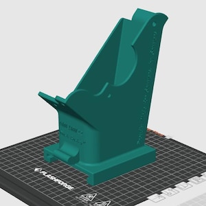 May include: A teal 3D-printed phone stand with a curved design. The stand has a base with the text "FLASHFORGE" and other text. The stand is designed to hold a phone upright.
